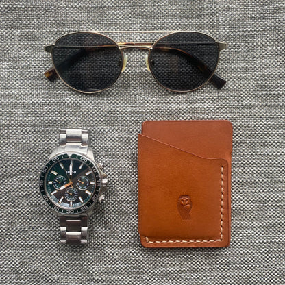 Handmade leather cardholder in windsor tan, among a collection of luxury items